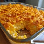 Close-up of a creamy, cheesy potato bake in a glass dish, featuring a golden, crunchy cornflake topping.