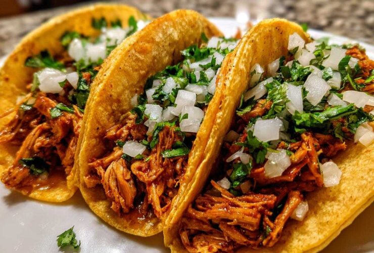 Close-up of three street-style chicken tacos filled with shredded meat, topped with diced white onion and fresh cilantro.