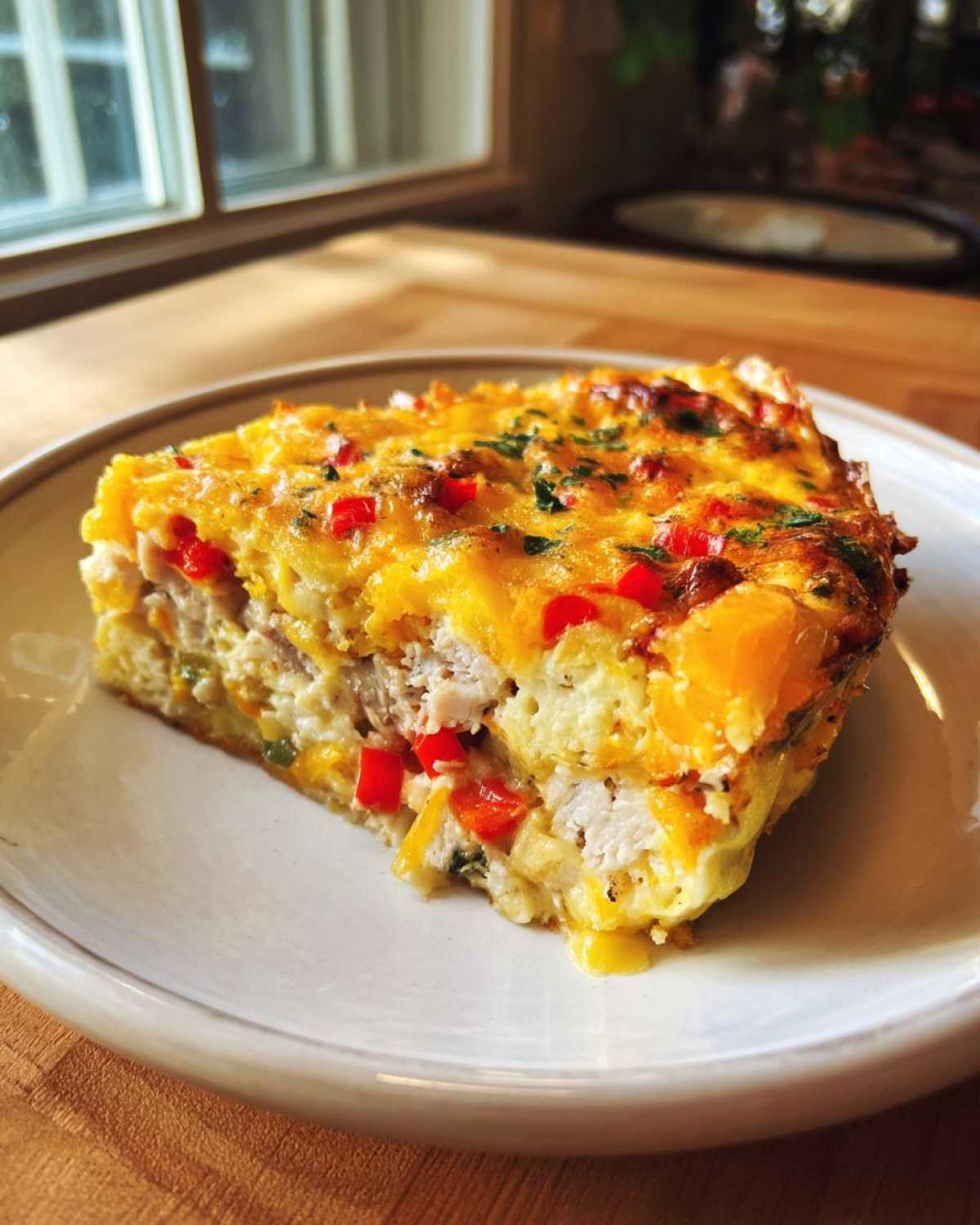 A thick slice of savory egg bake featuring chunks of chicken, red peppers, and melted cheese topping.