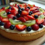 Close-up of a fruit pizza sugar cookie base topped with white frosting, sliced strawberries, kiwi, and blueberries.