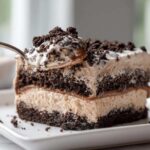 A spoonful of creamy Oreo dirt cake being lifted from a layered slice on a white plate.