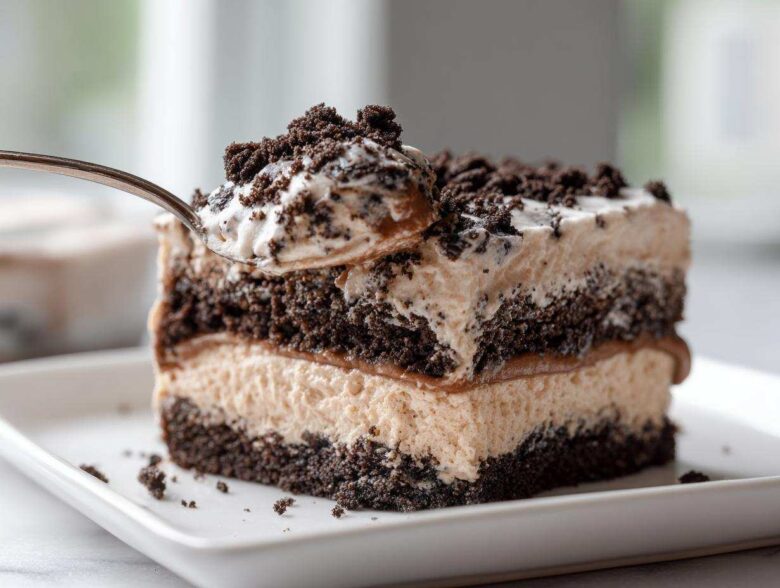 A spoonful of creamy Oreo dirt cake being lifted from a layered slice on a white plate.