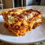 A thick, square slice of baked pasta layered with rich meat sauce and melted, browned cheese, ready to eat in this amazing pasta bake.