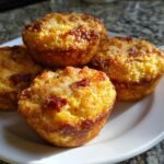 Four golden brown, freshly baked pizza muffins piled on a white plate.