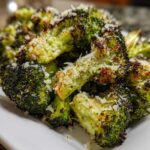 Close-up of crispy, charred roasted broccoli florets topped generously with grated Parmesan cheese.