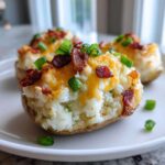 A close-up of an amazing twice baked potato stuffed with creamy filling, topped with melted cheddar cheese, bacon bits, and green onions.
