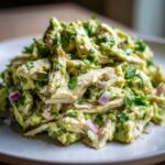 Close-up of shredded chicken mixed with creamy avocado dressing, red onion, and cilantro in avocado chicken salad.