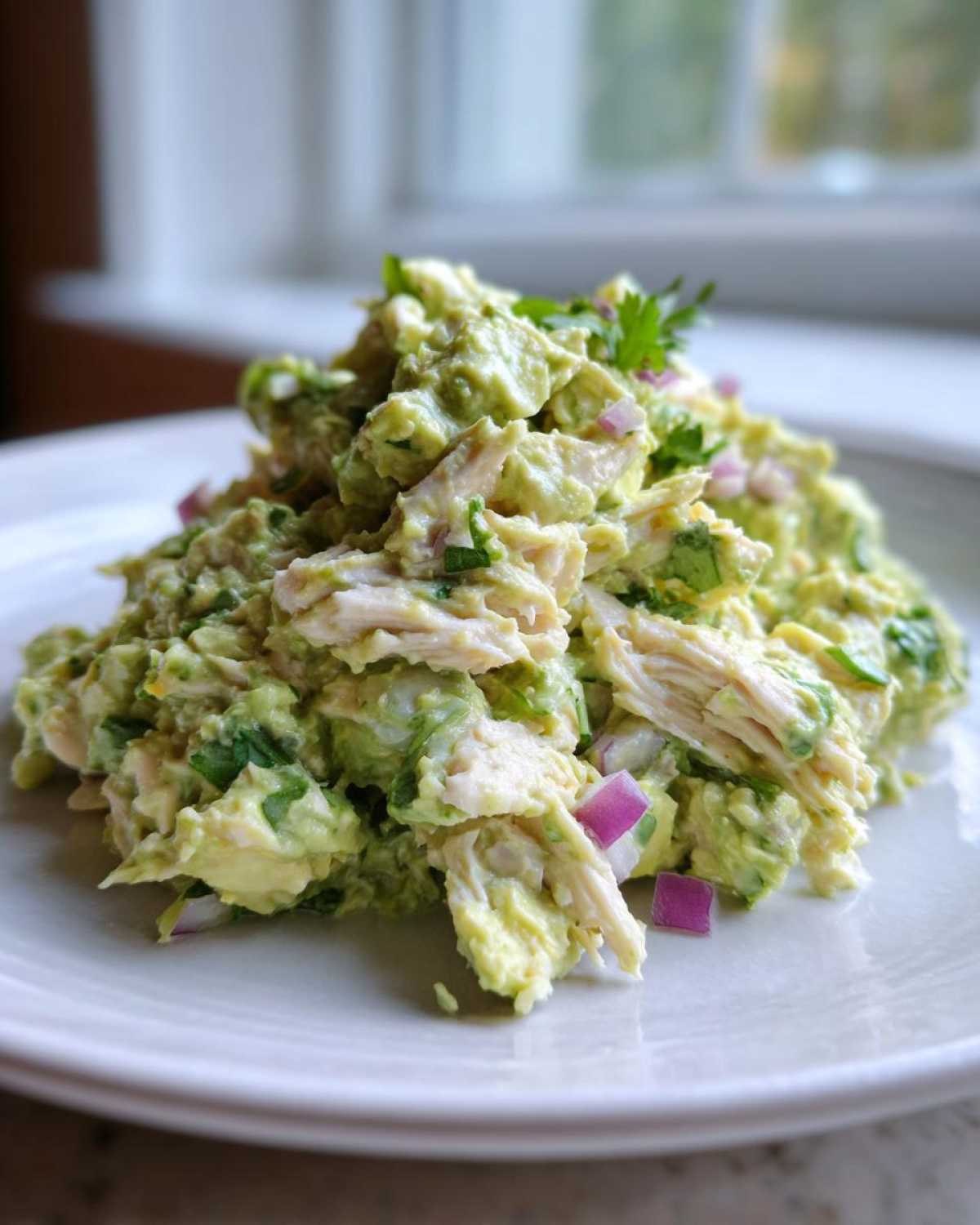 A mound of creamy avocado chicken salad mixed with red onion and cilantro, garnished with parsley.