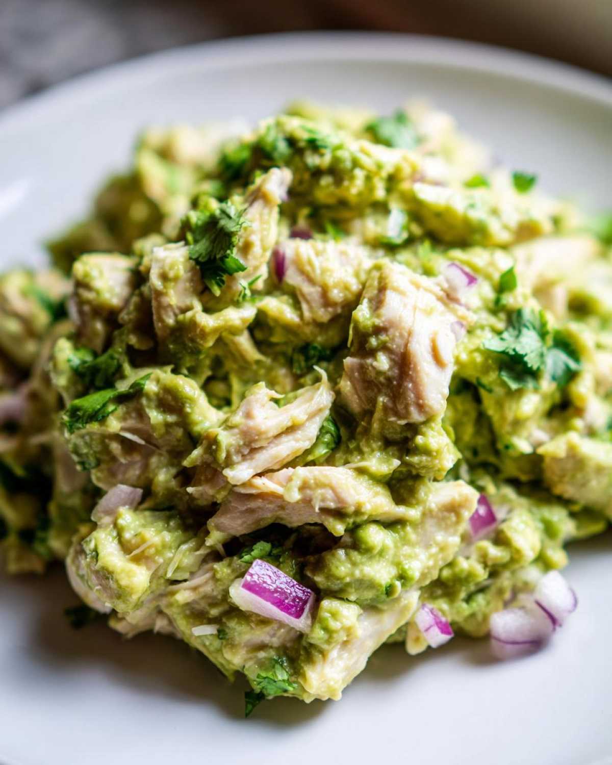 Close-up of creamy avocado chicken salad mixed with chunks of chicken, red onion, and cilantro.