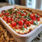 Close-up of a baked 3-cheese bruschetta dip topped with fresh diced tomatoes and basil.