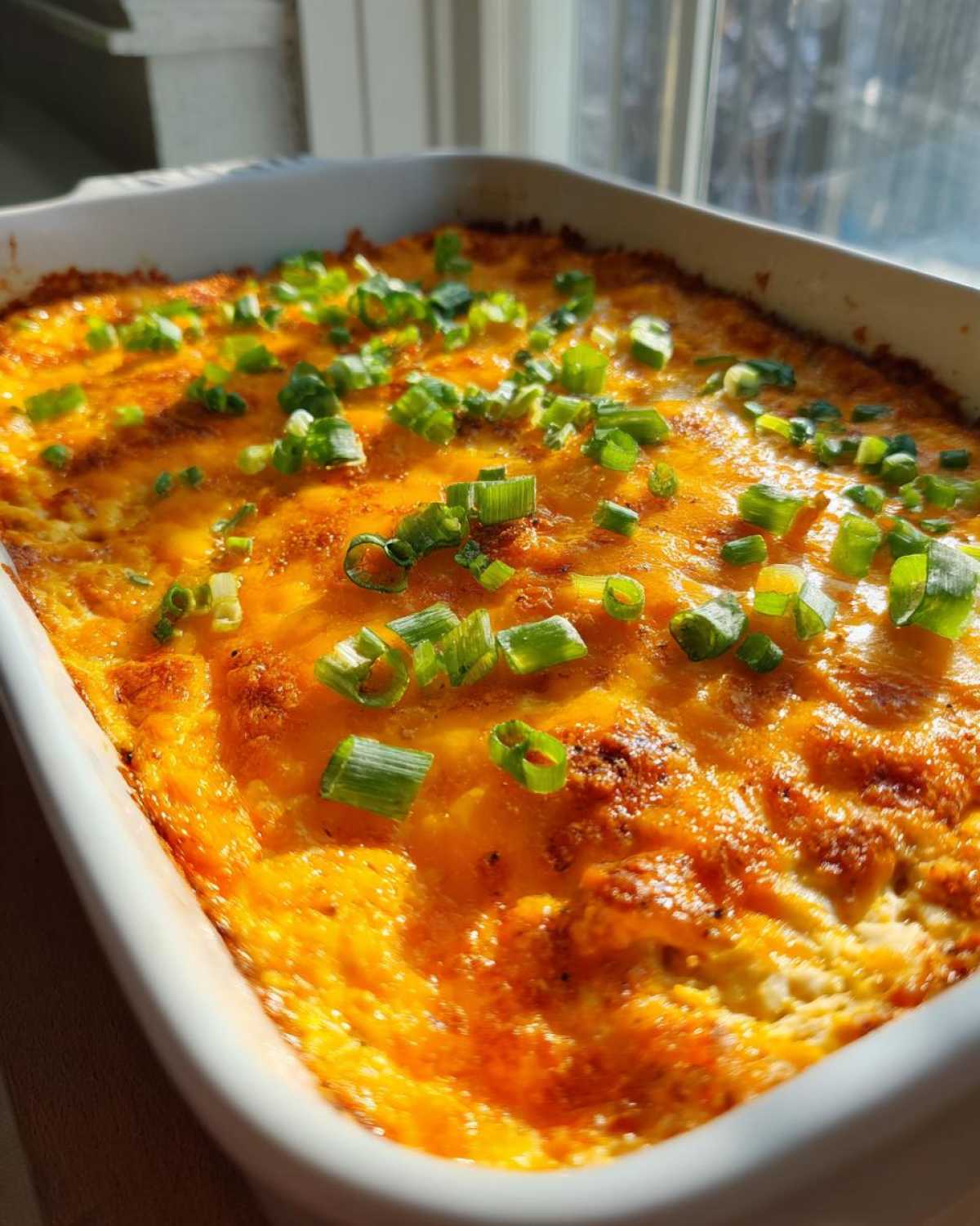 Close-up of a hot, baked Buffalo chicken dip topped with melted orange cheese and fresh green onions.