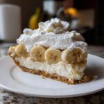 A generous slice of banana cream pie recipe featuring a graham cracker crust, creamy filling, banana slices, and whipped cream topping.