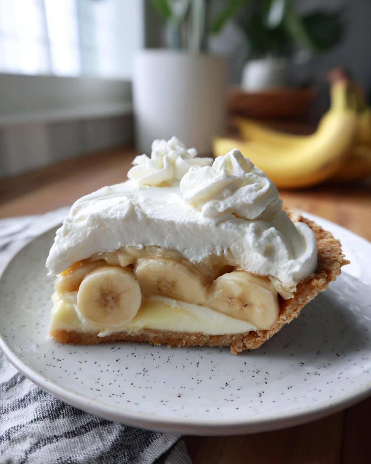 A thick slice of banana cream pie recipe showing layers of crust, custard, sliced bananas, and whipped cream.