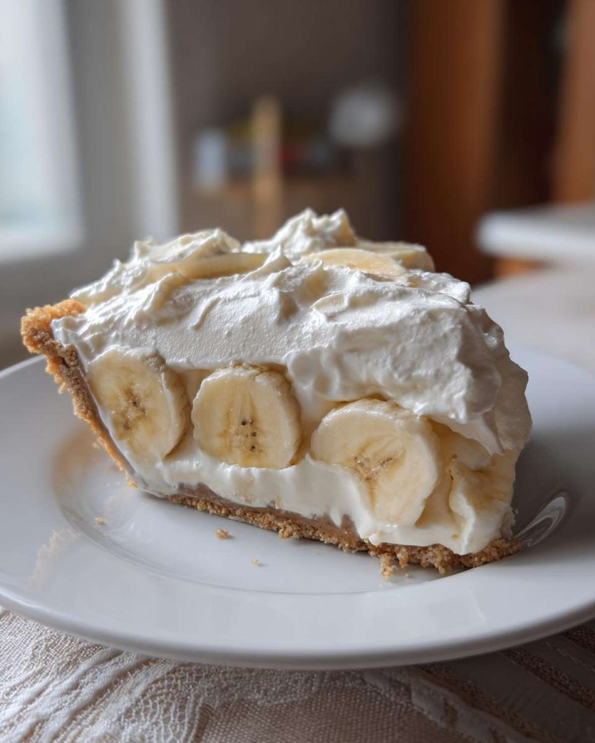 A close-up of a perfect slice of banana cream pie recipe showing layers of crust, bananas, and whipped cream.