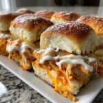 Close-up of cheesy buffalo chicken sliders on Hawaiian rolls, drizzled with ranch or blue cheese dressing.