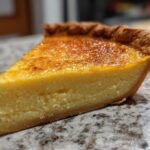 Close-up of a thick slice of buttermilk pie showing the creamy yellow filling and golden-brown crust.