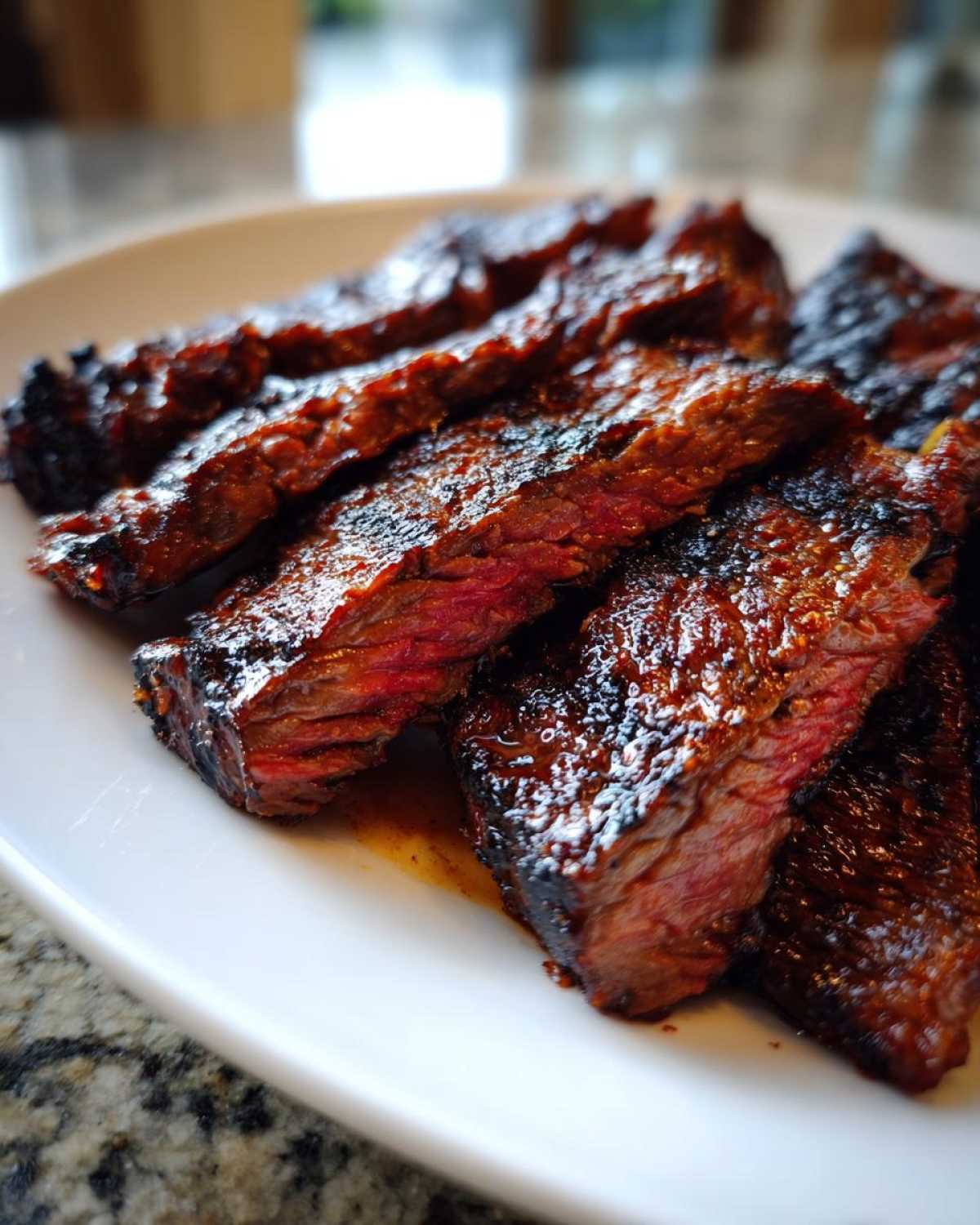 Close-up of sliced, grilled steak showing a medium-rare center, coated in a rich, dark Carne asada marinade.