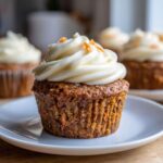 Close-up of a single carrot cake muffin topped with a swirl of cream cheese frosting and orange zest.