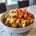 A close-up of a delicious cheeseburger bowl featuring seasoned ground beef, melted cheese, pickles, tomatoes, onions, and a drizzle of sauce.
