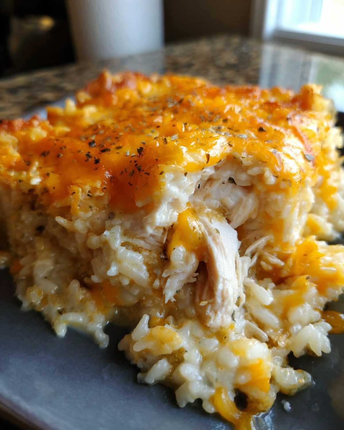 Close-up of a serving of cheesy chicken and rice casserole showing shredded chicken mixed with creamy rice and topped with melted cheddar cheese.