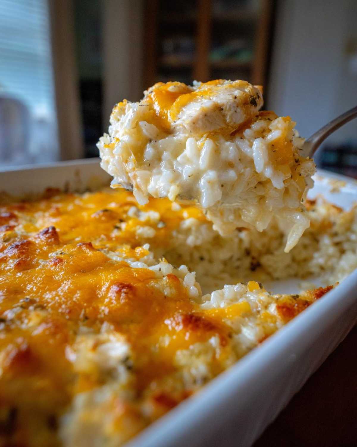 A spoonful of creamy, cheesy chicken and rice being lifted from a white baking dish.