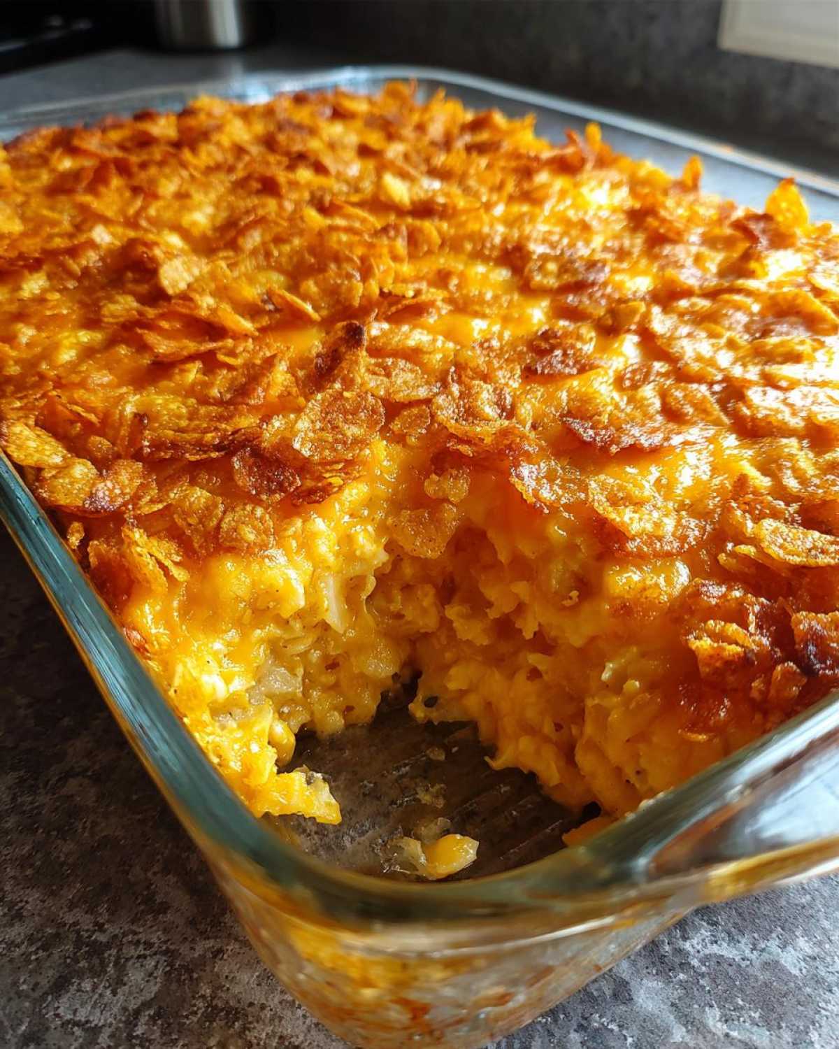 Close-up of a baked cheesy potato casserole in a glass dish with a golden, crunchy cornflake topping.