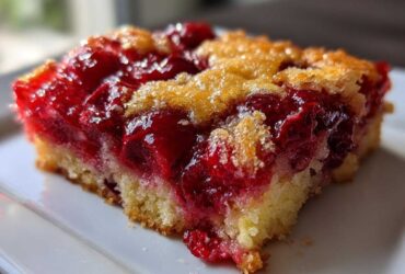 Close-up of a moist slice of cherry dump cake showing bright red cherry filling and a golden, slightly crumbly topping.