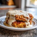 Two crispy, golden brown chicken fried steak portions stacked and smothered in creamy white pepper gravy.