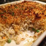 Close-up of a baked chicken wild rice casserole with a crispy, golden breadcrumb topping and visible creamy filling with peas.