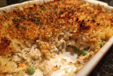 Close-up of a baked chicken wild rice casserole with a crispy, golden breadcrumb topping and visible creamy filling with peas.