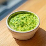 Close-up of vibrant, creamy cilantro lime sauce speckled with fresh herbs in a small white ramekin.