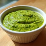 A vibrant, thick cilantro lime sauce filling a small white ramekin, set on a wooden surface.