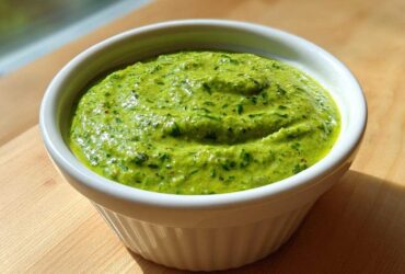 A vibrant, thick cilantro lime sauce filling a small white ramekin, set on a wooden surface.