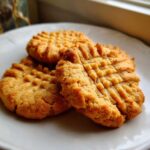 Close-up of three golden brown peanut butter cookies with classic crisscross fork marks on a white plate.