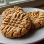 Close-up of three perfectly baked peanut butter cookies featuring the classic crisscross fork marks, resting on a white plate.