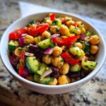 Close-up of a vibrant high protein bean salad featuring chickpeas, cucumbers, red peppers, and red onion in a white bowl.