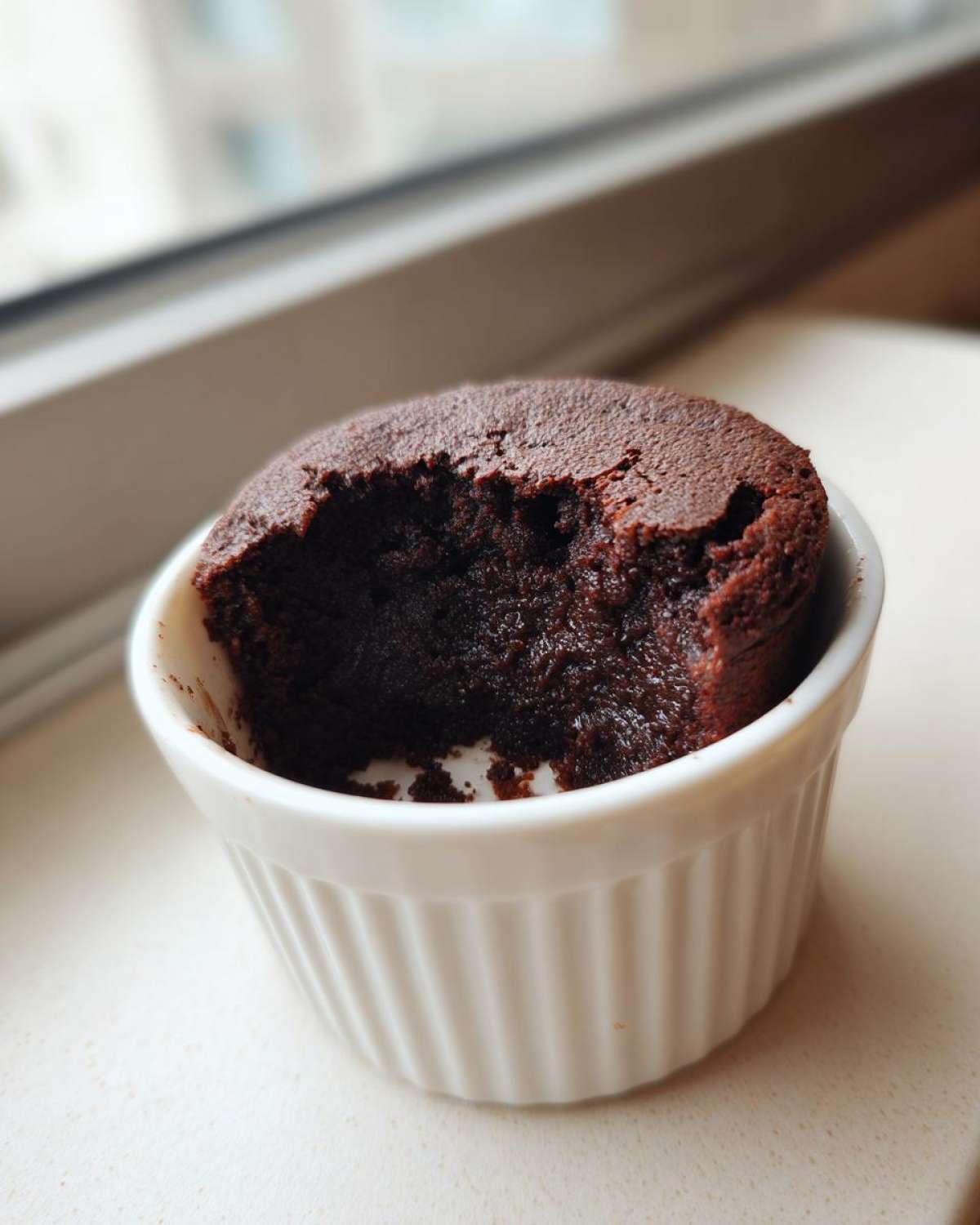 A rich, dark chocolate Cottage Cheese Microwave Brownie with a bite taken out, served in a white fluted ramekin.
