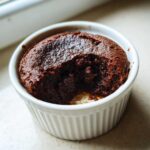 A close-up of a rich, dark chocolate Cottage Cheese Microwave Brownie with a bite taken out, served in a white ramekin.