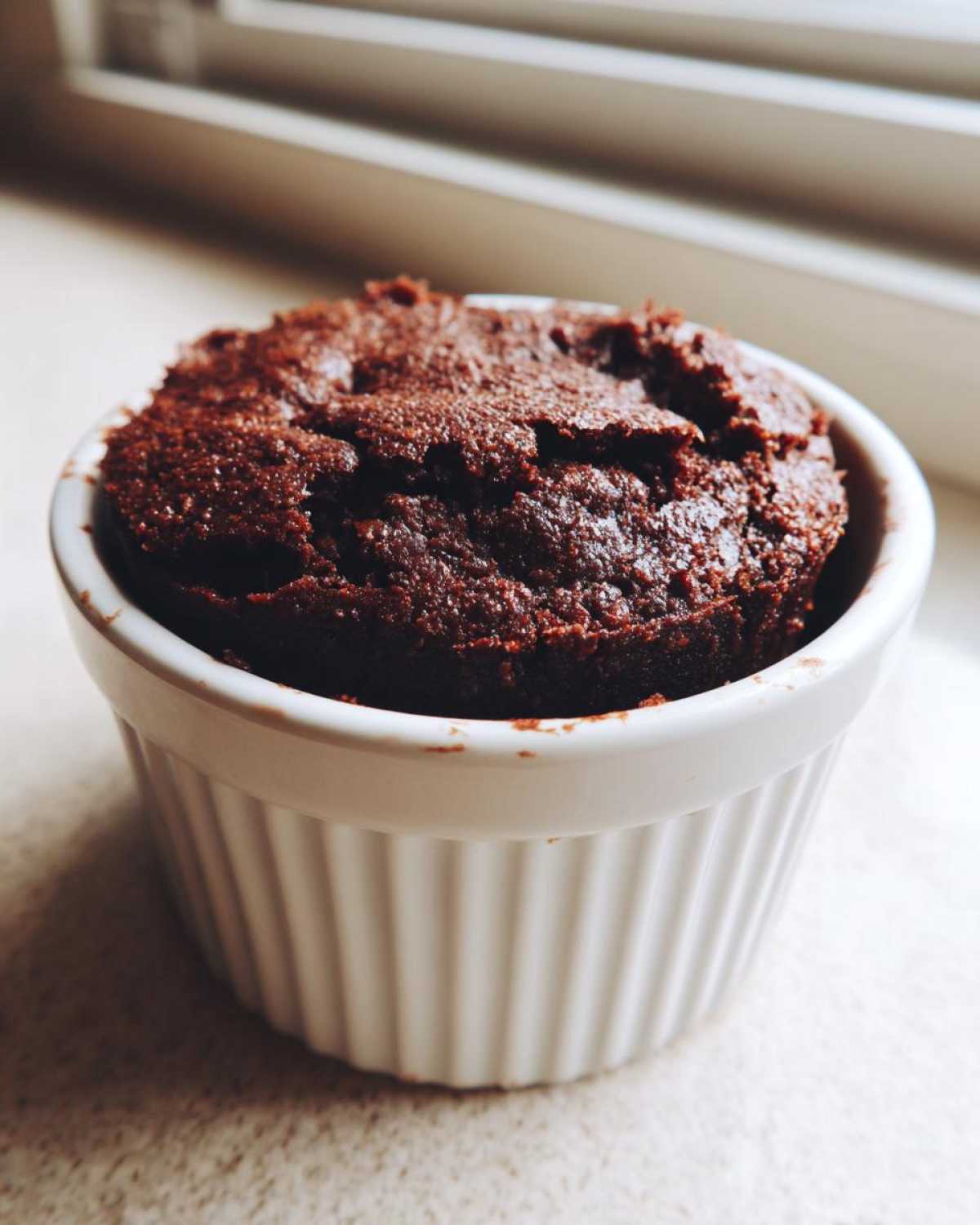 A rich, dark chocolate Cottage Cheese Microwave Brownie baked perfectly in a white, fluted ramekin.