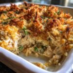Close-up of a scoop taken from a creamy chicken wild rice casserole topped with golden brown crispy breadcrumbs and peas.