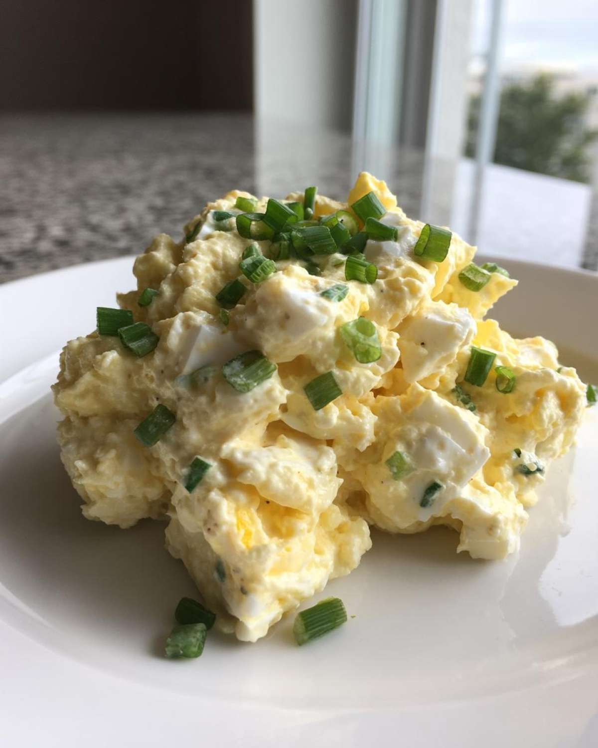 A close-up serving of creamy egg salad recipe garnished with fresh chopped chives on a white plate.