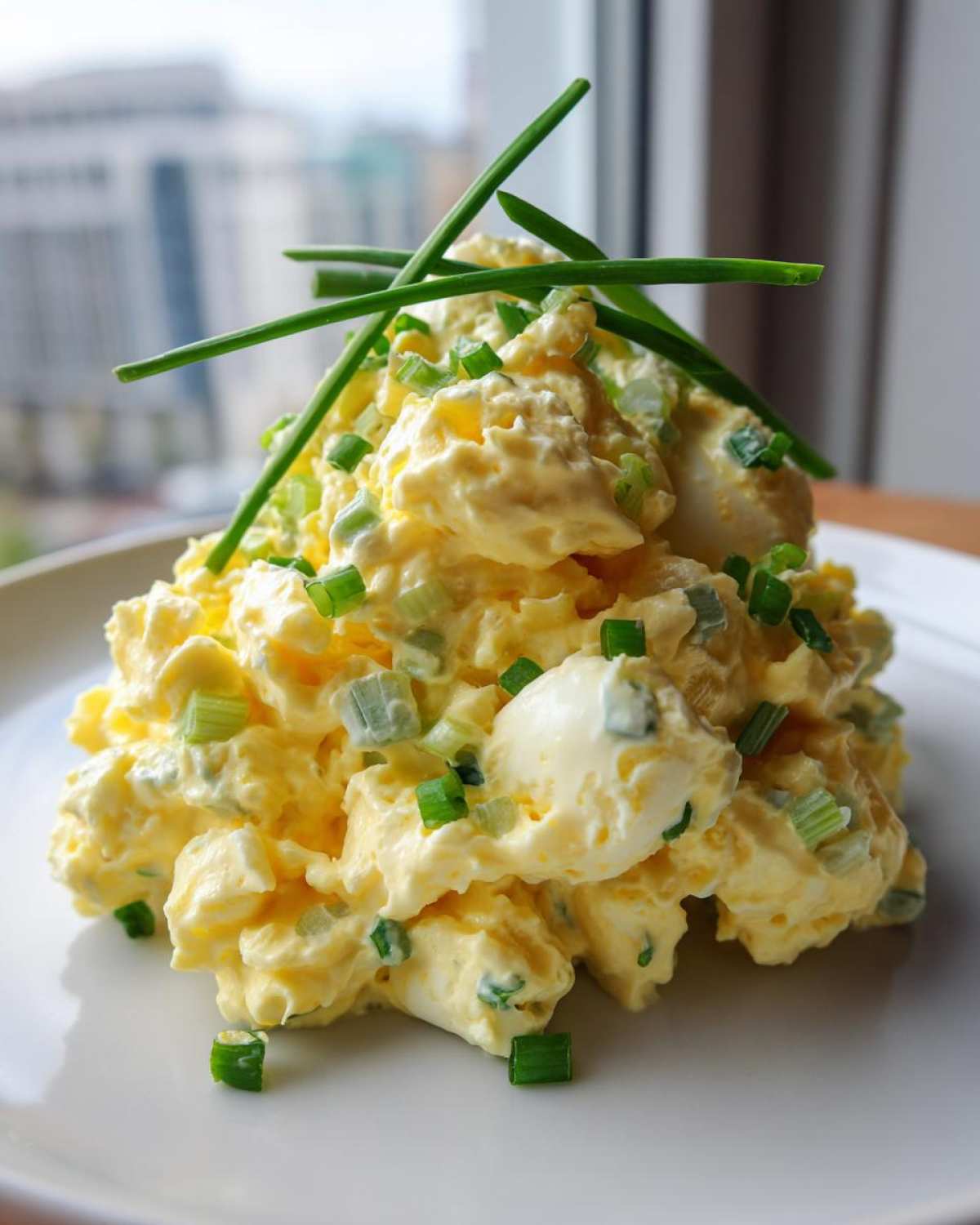A beautifully plated mound of creamy egg salad recipe, garnished with fresh chopped chives and whole chive stalks.