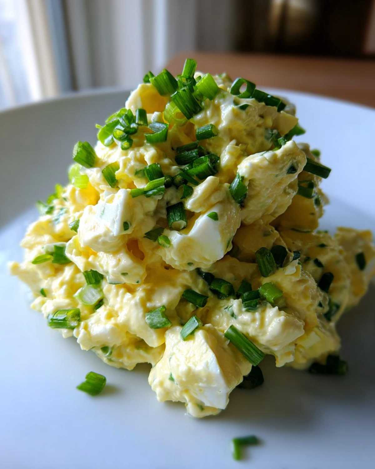 A mound of creamy, yellow egg salad recipe generously topped with freshly chopped green chives on a white plate.