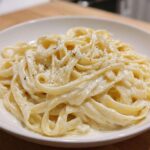 Close-up of fettuccine pasta generously coated in rich homemade alfredo sauce and topped with cracked black pepper.