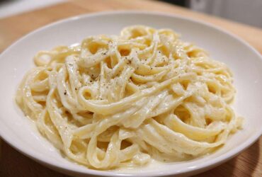 Close-up of fettuccine pasta generously coated in rich homemade alfredo sauce and topped with cracked black pepper.