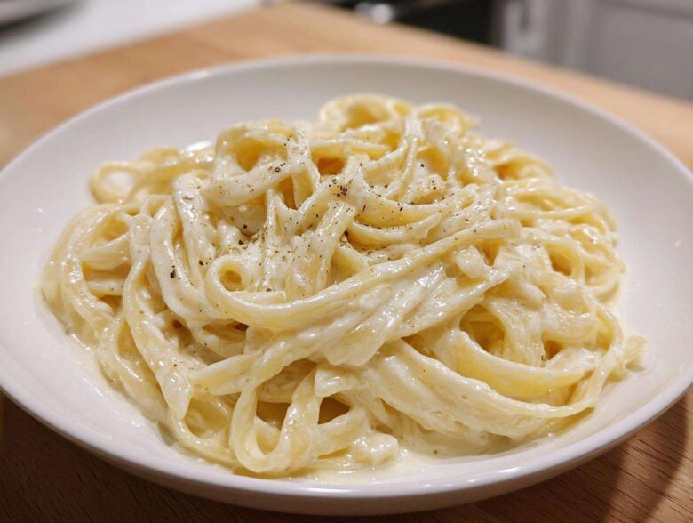 Close-up of fettuccine pasta generously coated in rich homemade alfredo sauce and topped with cracked black pepper.