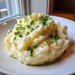 A fluffy mound of creamy garlic mashed potatoes garnished with fresh chopped chives and black pepper.