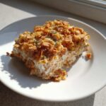 A square serving of creamy hot chicken salad topped with a thick layer of crunchy, golden cornflakes.