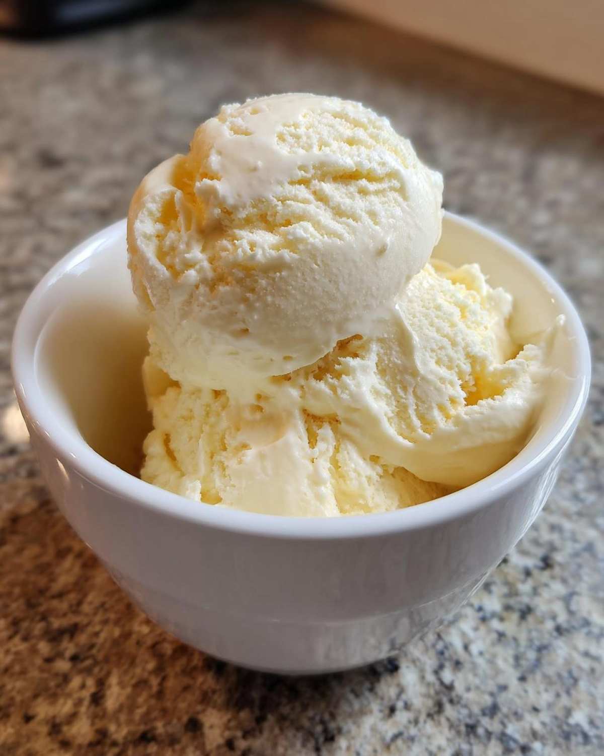 Two scoops of creamy, pale yellow protein ice cream served in a small white bowl.