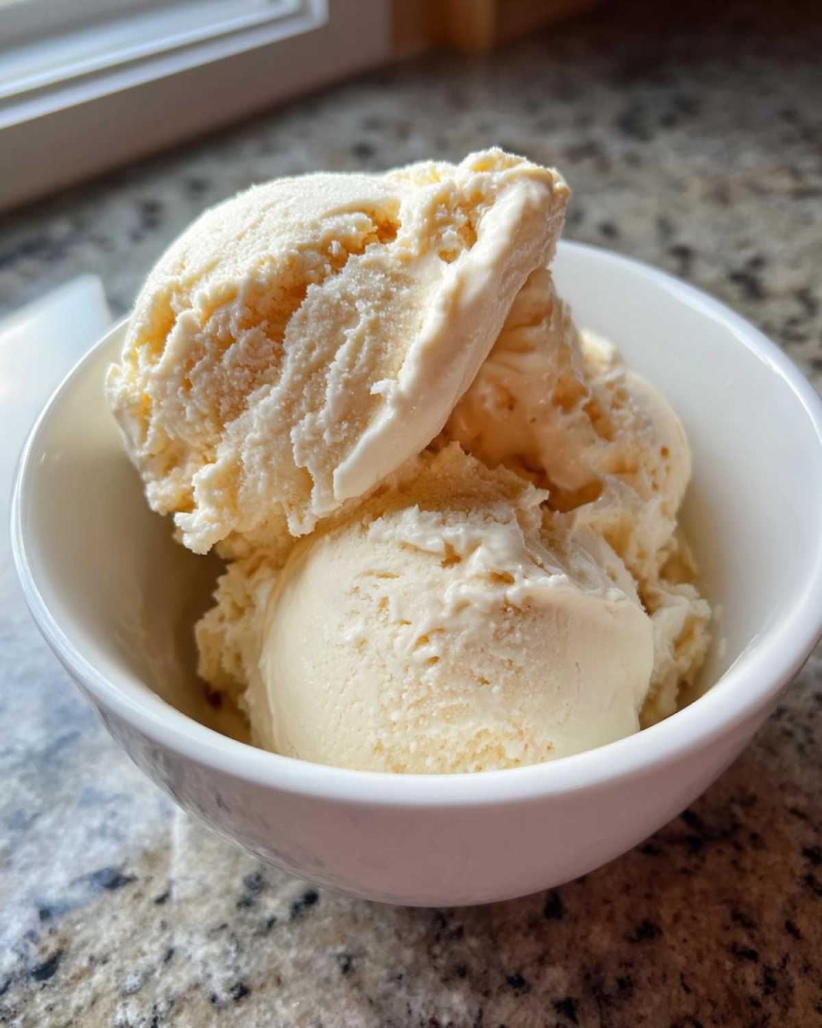 Close-up of three scoops of creamy, vanilla-colored protein ice cream served in a small white bowl.